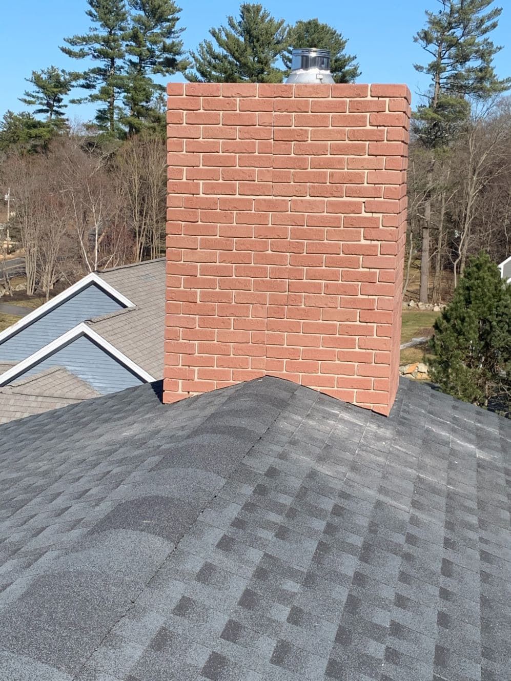 Freshly rebuilt brick chimney rising past a shingle roof