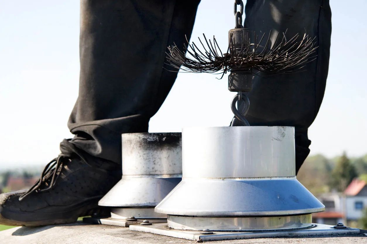 Whip brush lowered between two steel flue collars on a chimney top