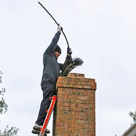 Technician on a ladder working rods into a brick chimney